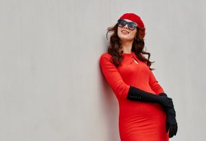 Beautiful woman in red dress, sun glasses, beret near the white wall